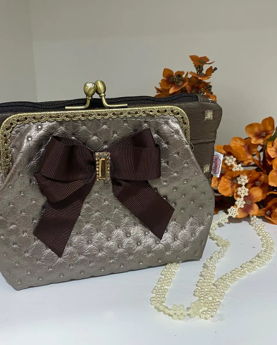 Bolsa de boquilha prateada acolchoada com laço castanho.