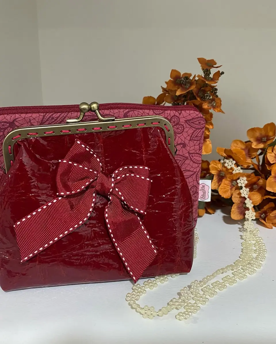 Bolsa de boquilha em verniz vinho com laço de pesponto branco.