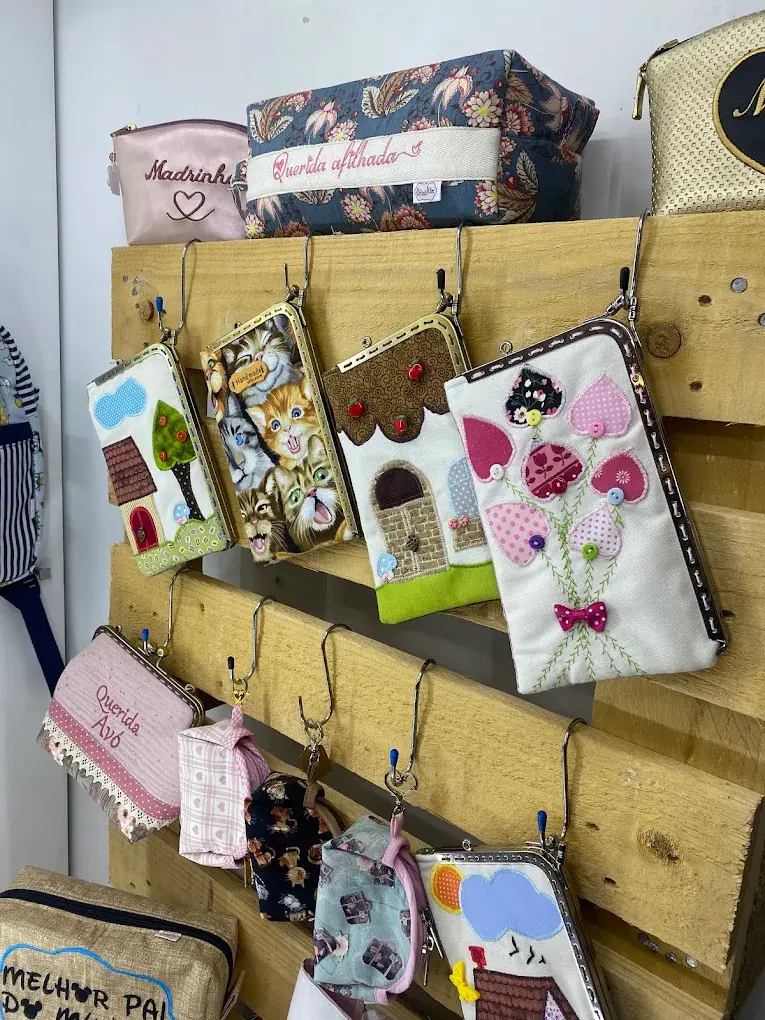 Bolsinhas e porta-moedas pendurados num expositor de madeira, com aplicações de casinhas, joaninhas e flores.
