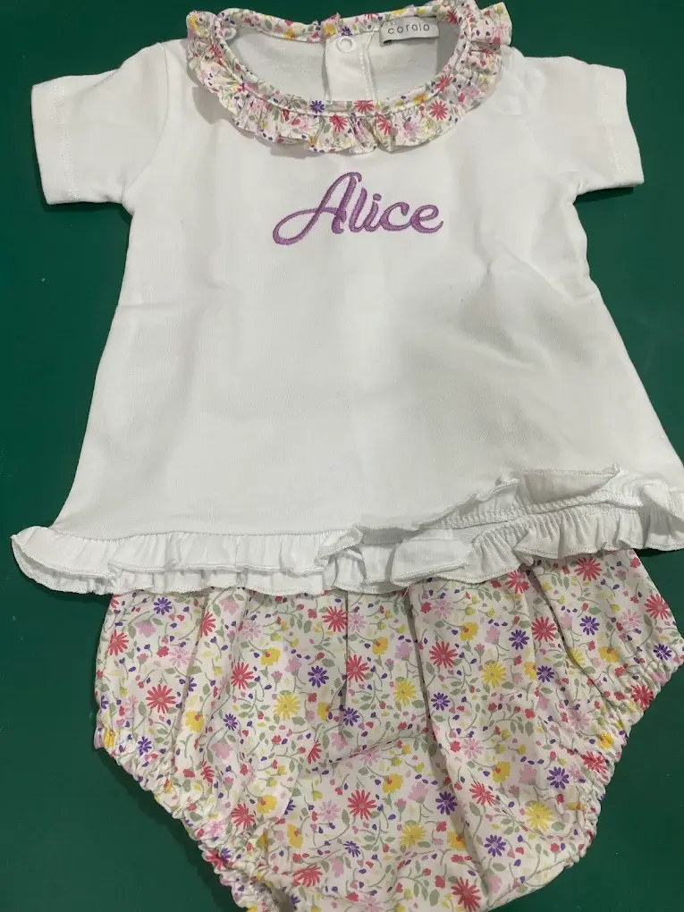 Blusa branca com gola de folhos florais e o nome Alice bordado a lilás, com calção de tecido floral.
