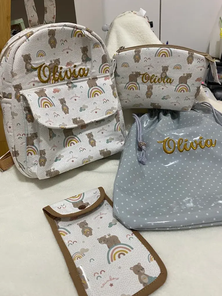 Mochila, necessaires e porta-documentos em tecido de ursos e arco-íris, com o nome Olivia bordado a dourado.