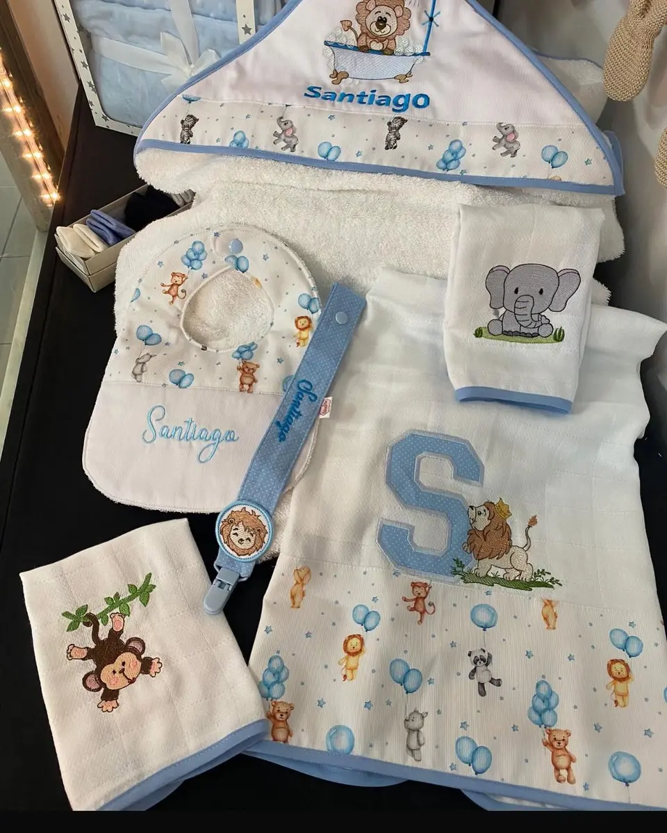 Conjunto de bebé com o nome Santiago bordado a azul: babete, fralda, prendedor de chupeta e toalha.