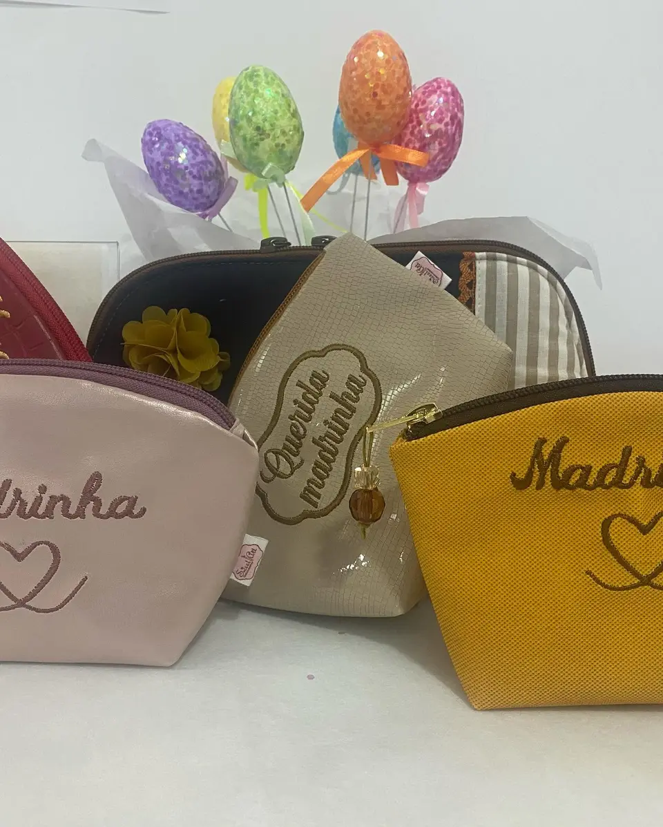 Necessaires em rosa, bege e mostarda com as palavras Madrinha e Querida madrinha bordadas.