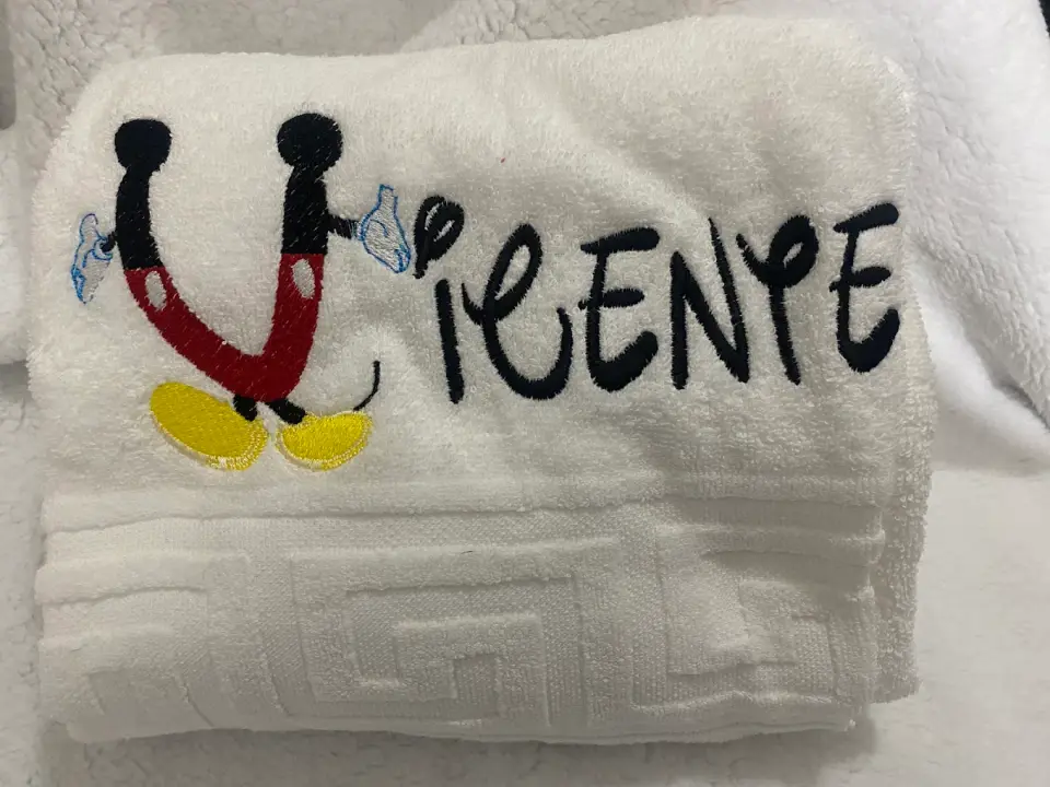 Toalha de felpo branca com o nome Vicente bordado e a inicial desenhada com as mãos e os pés do Mickey.